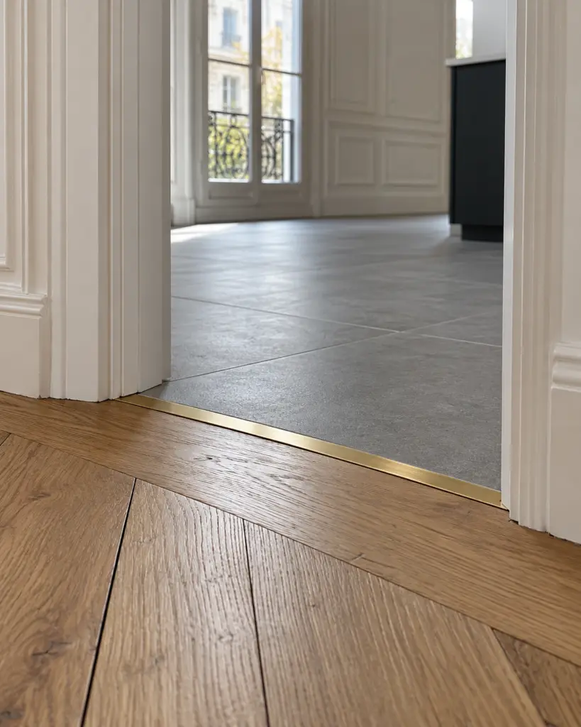 Seuil de porte en laiton posé à fleur entre un parquet chêne et un carrelage gris
